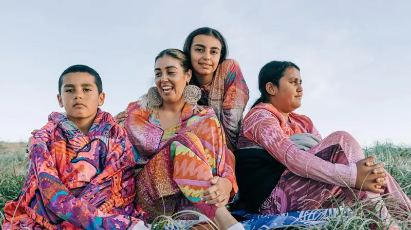 Renae Lamb with her three children on the dunes at Worimi Country, wrapped in Midnight Dreaming prints
